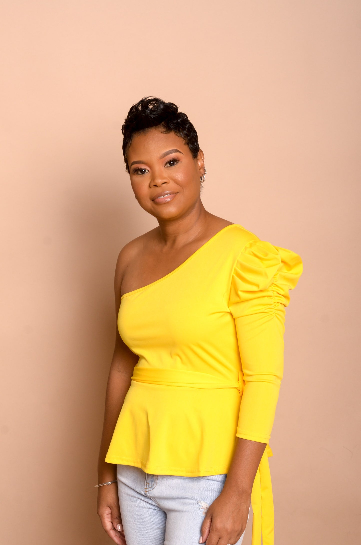 Model is wearing yellow peplum top and showing the left hand side with puff sleeve