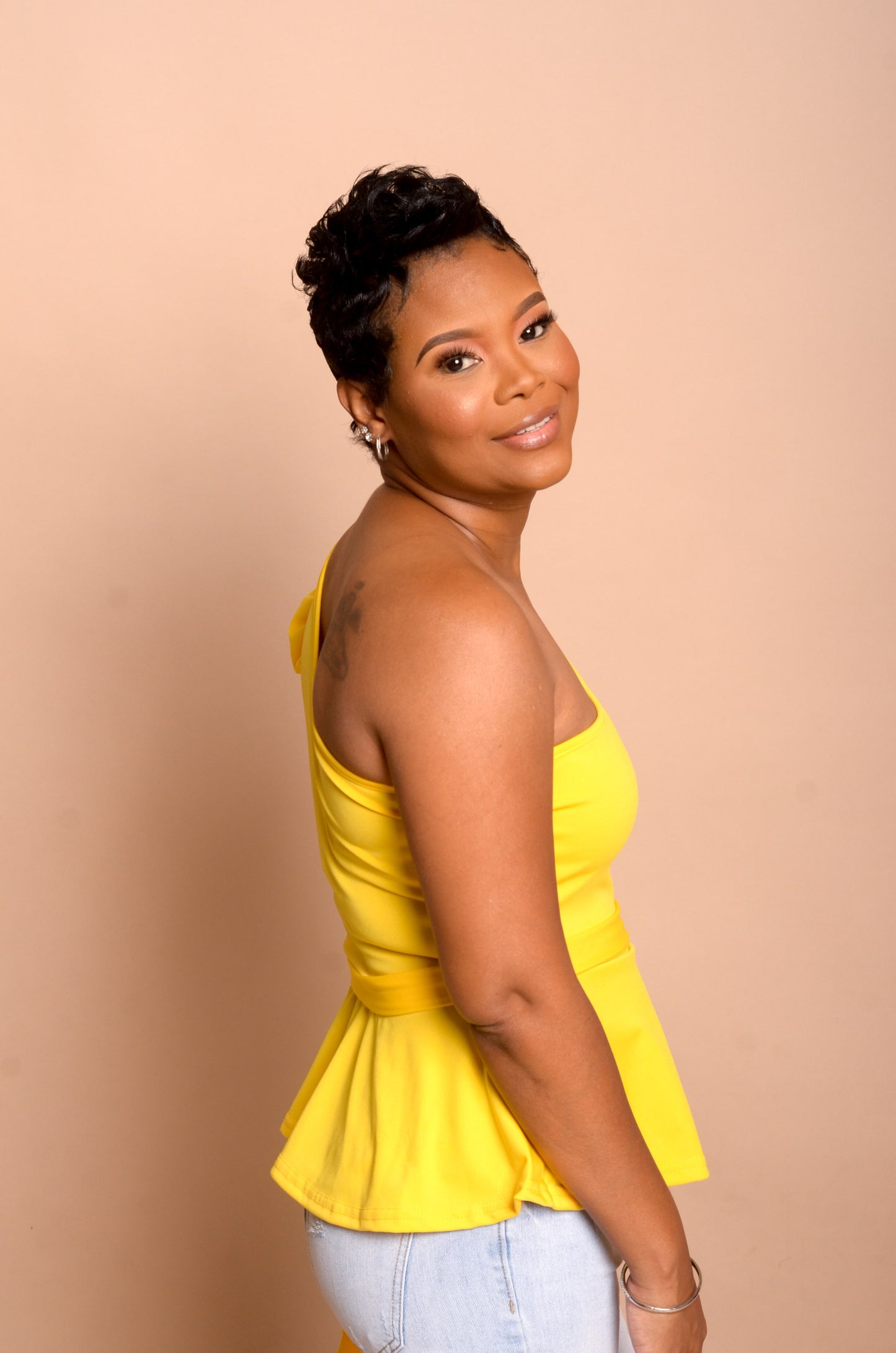 Model is wearing yellow peplum top and showing the right side without sleeve